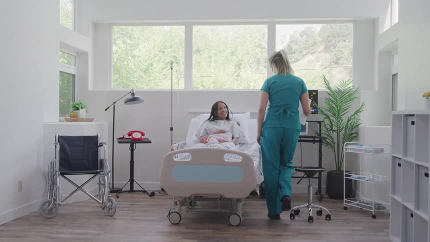 A nurse speaks with a patient resting in a modern sunlit hospital room