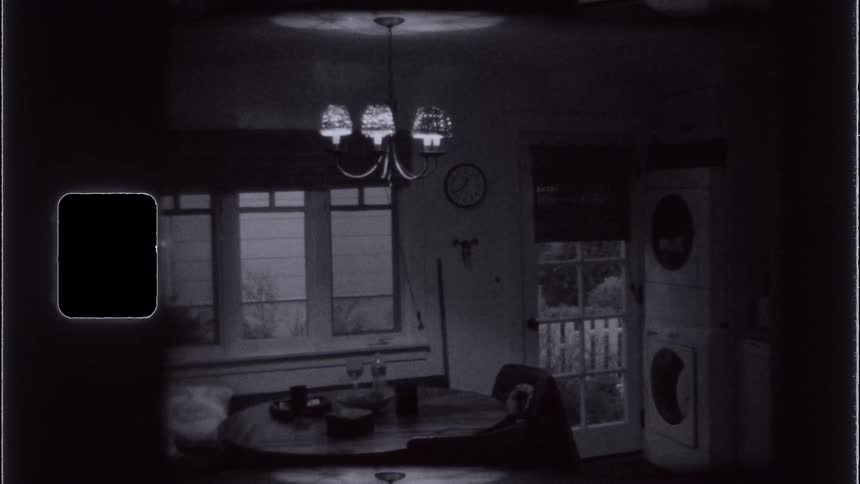 A dimly lit vintage kitchen is captured in a grainy black and white frame