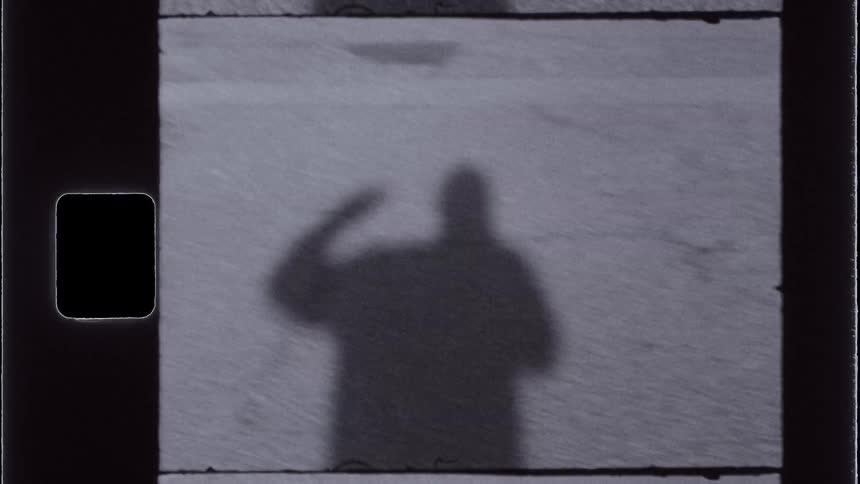 Vintage footage of a persons shadow on the asphalt waving hello