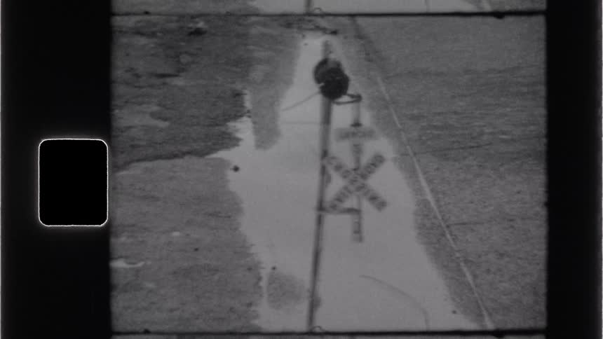 A black and white image framed with rounded corners shows a flooded road with a railroad crossing sign