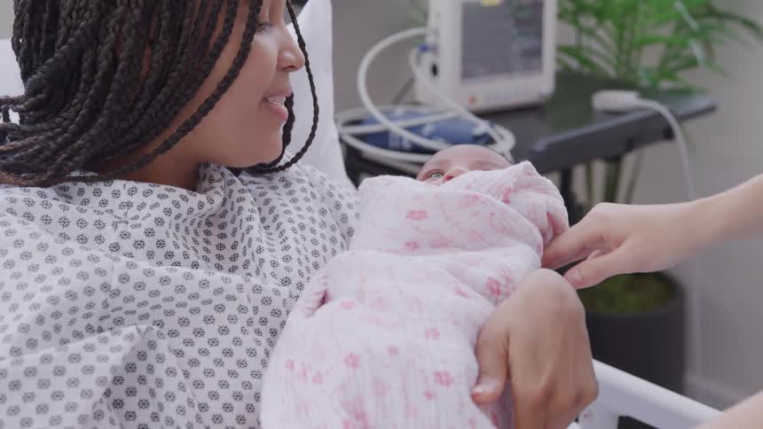 A woman in a hospital gown holds a swaddled baby she has just received