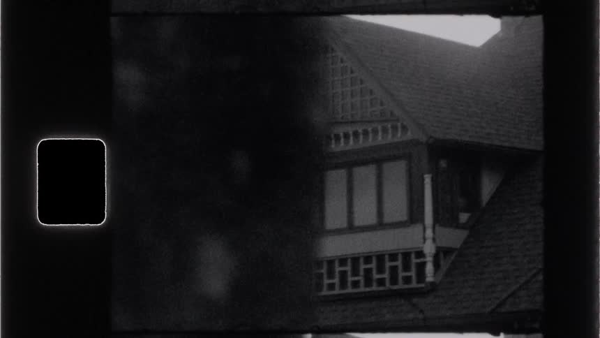 Black and white archival shot of a house upper story through a film frame