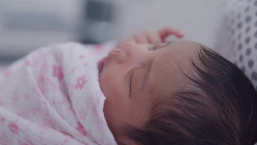 Newborn baby with eyes closed and moving hand