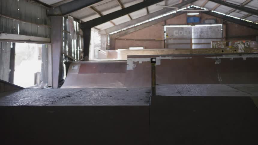 An indoor skatepark features various wooden ramps and structures under a metal ceiling