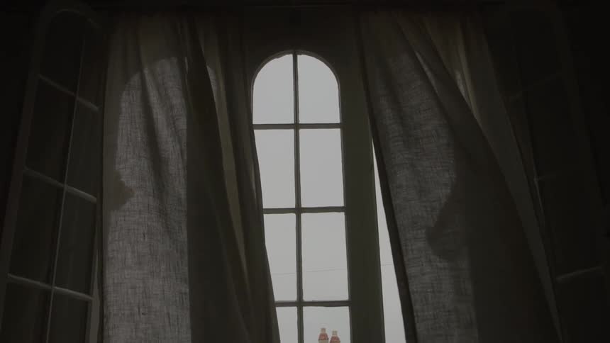 Sheer curtains part to reveal a tall arched window in soft daylight