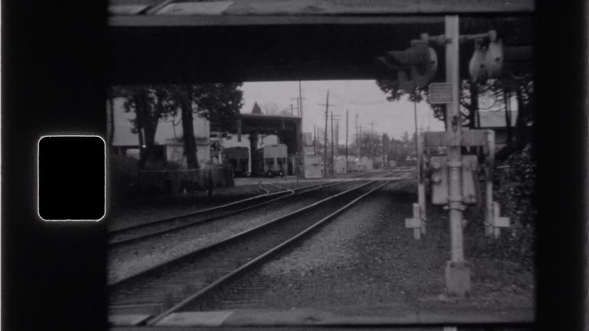 A black and white archival shot shows empty railroad tracks leading under a bridge