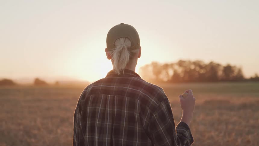 A woman looking at the sun wearing a long plaid shirt and a baseball cap