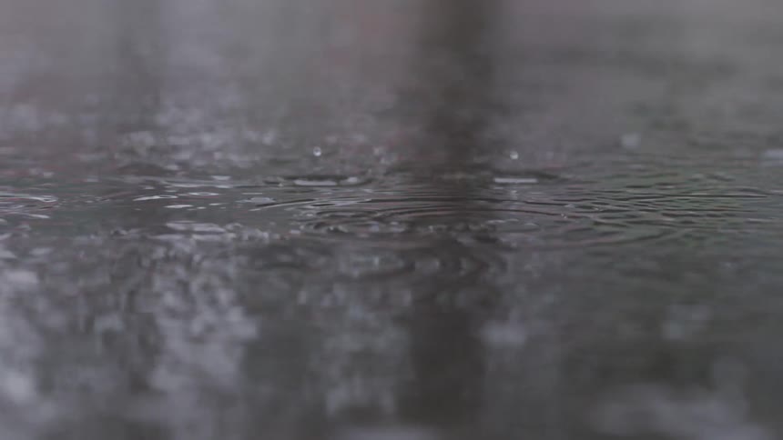 Close up of rain drops falling into a water puddle outdoors