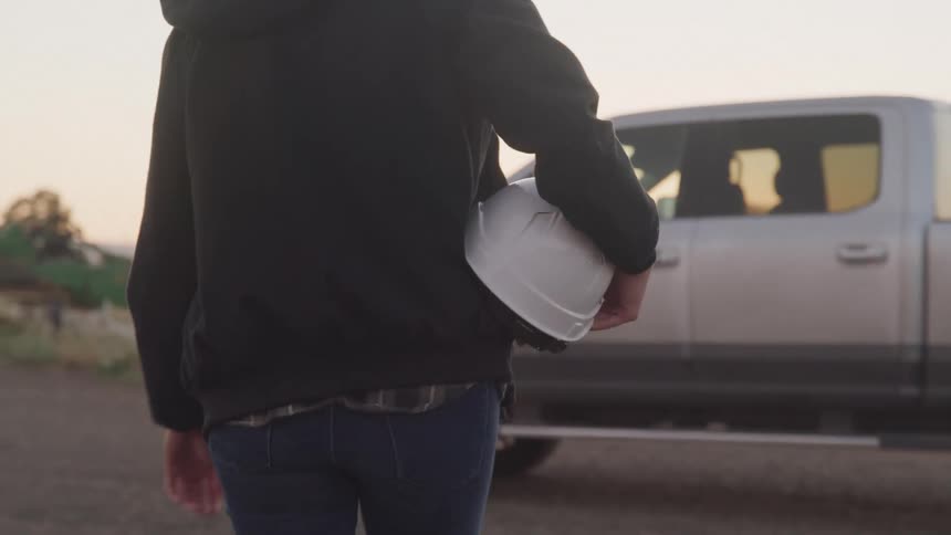 Back of a lady walking towards a parked truck holding an helmet at sunset
