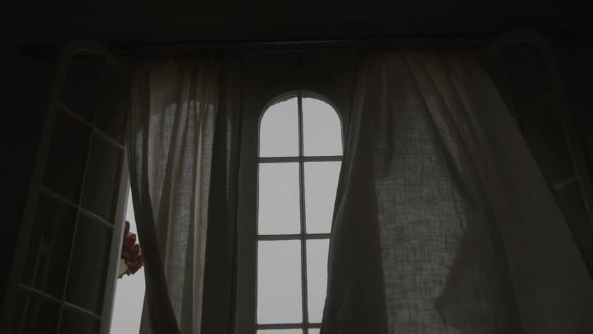 Soft light filters through sheer curtains around an arched window