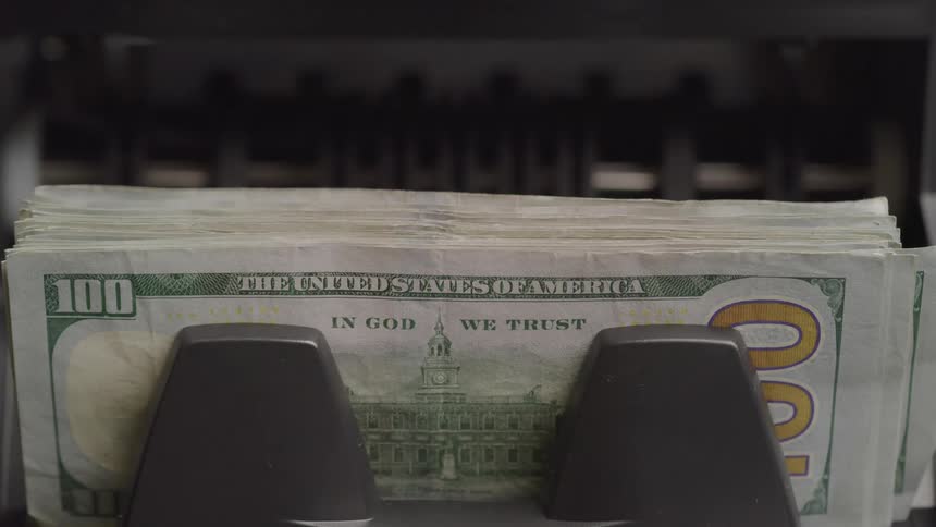 A stack of united states one hundred dollar bills is placed in a money counting machine