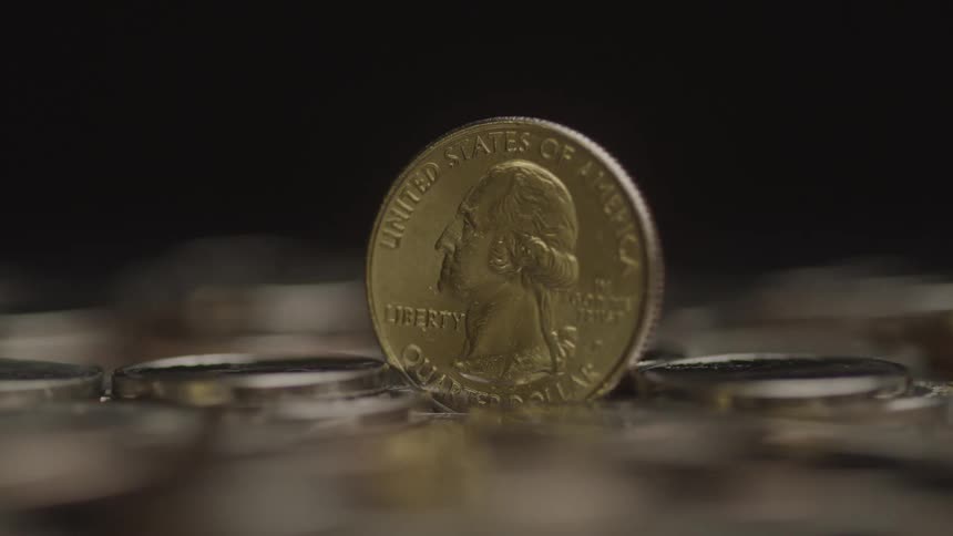 A u s quarter stands upright among a blurred pile of coins with dramatic lighting