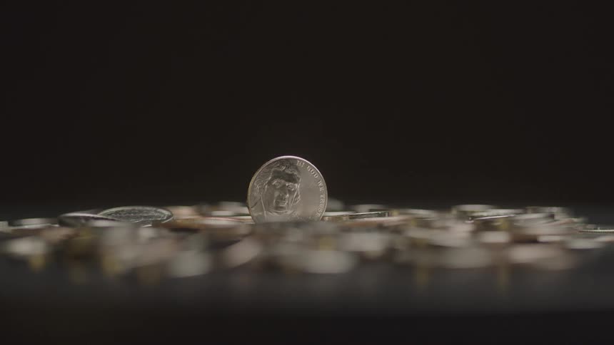 A single coin stands upright among a scattered pile of coins against a dark background