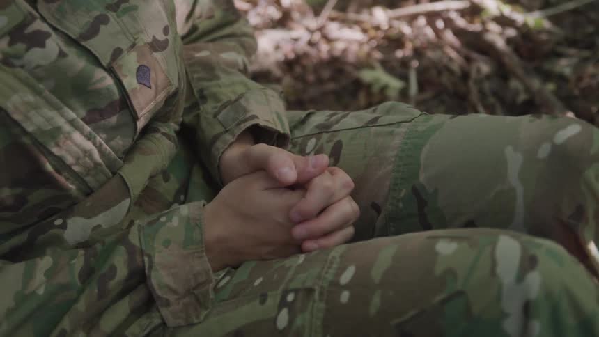 Person in military uniform with hands clasped sitting in the forest