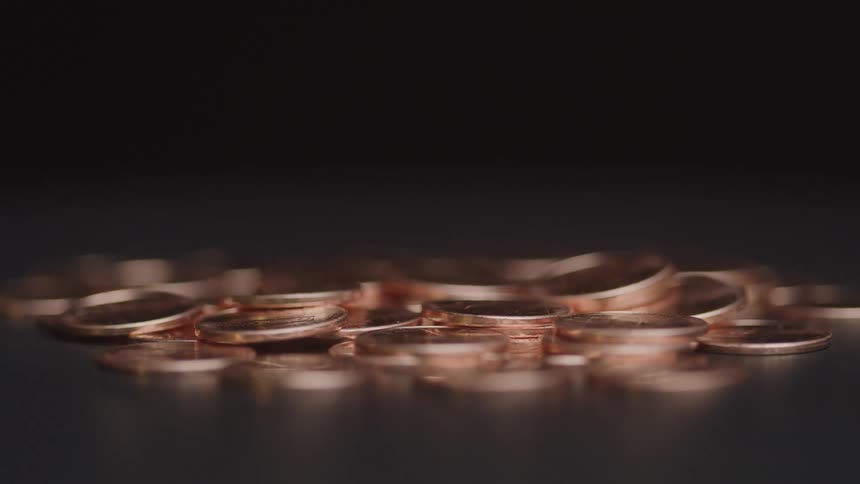 A scattered pile of coins lies on a dark surface in a low lit setting