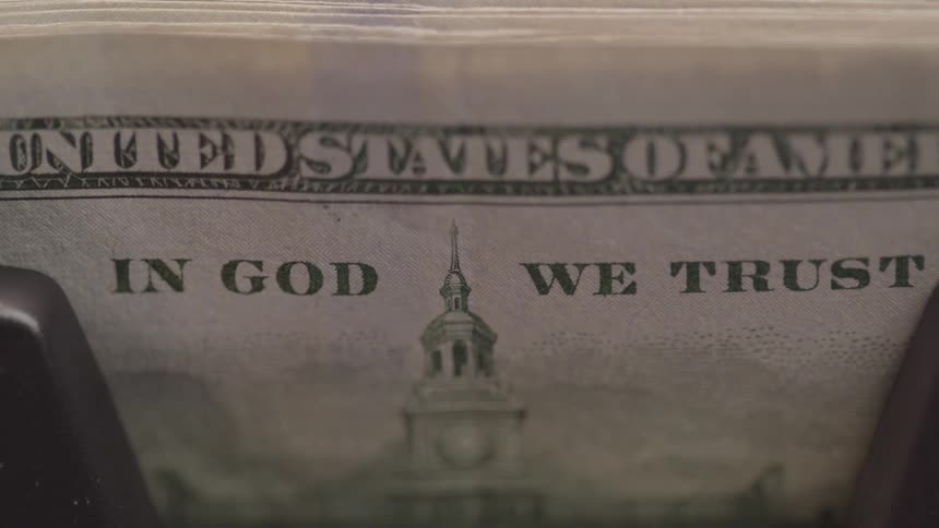 A bill counter counts usd bills revealing the text in god we trust on the money