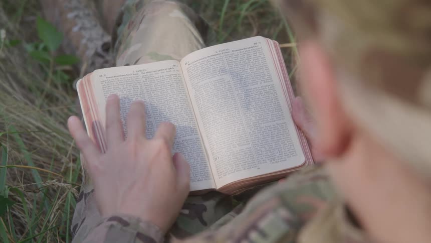 Person sitting in the woods outdoors and reading a bible