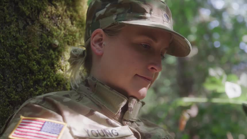 The soldier is writing while leaning against a tree