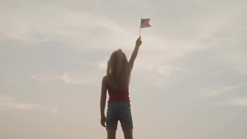 A girl is holding up a small american flag