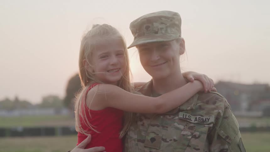 A smiling us army soldier hugs a young girl in a warm reunion at sunset