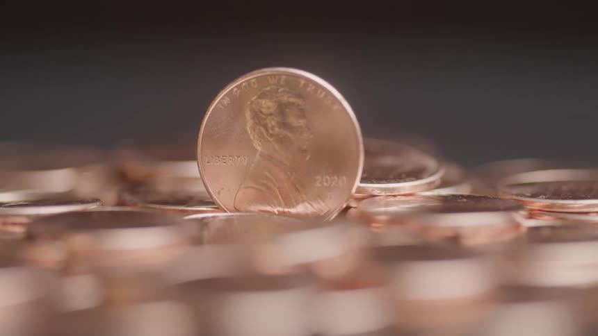 Close up of a bronze coin placed vertically in the middle of several other similar coins on a surface