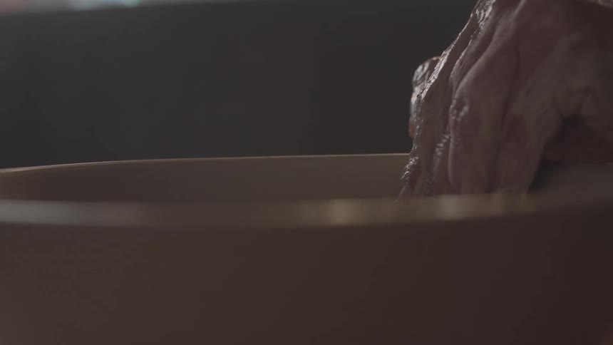 Close up of a person shaping pottery with their hand on a pottery wheel indoors