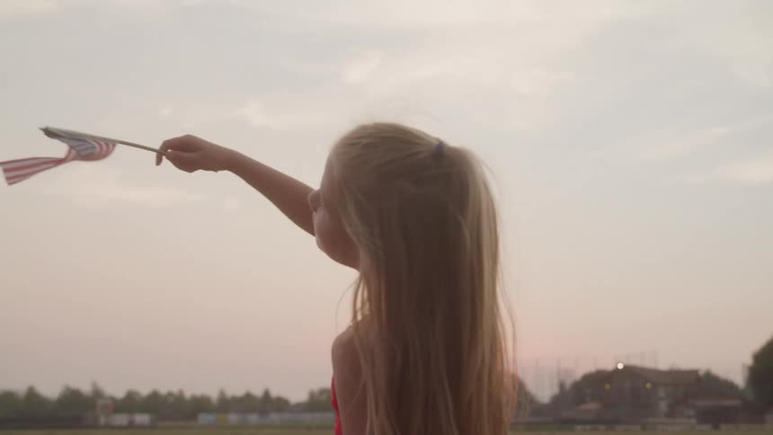 Girl waves a small american flag at sunset