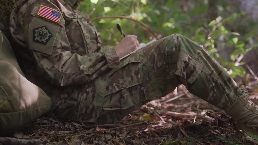 Woman in military uniform sitting in a forest writing