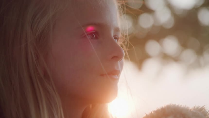 Sunlight highlights a child blonde hair as she stands in front of a warm softly blurred background with bokeh lights