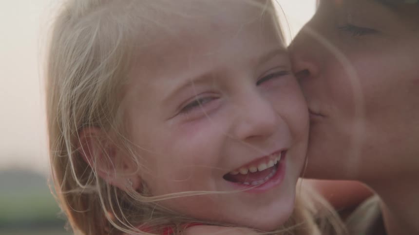 A mother kisses her daughter on the cheek