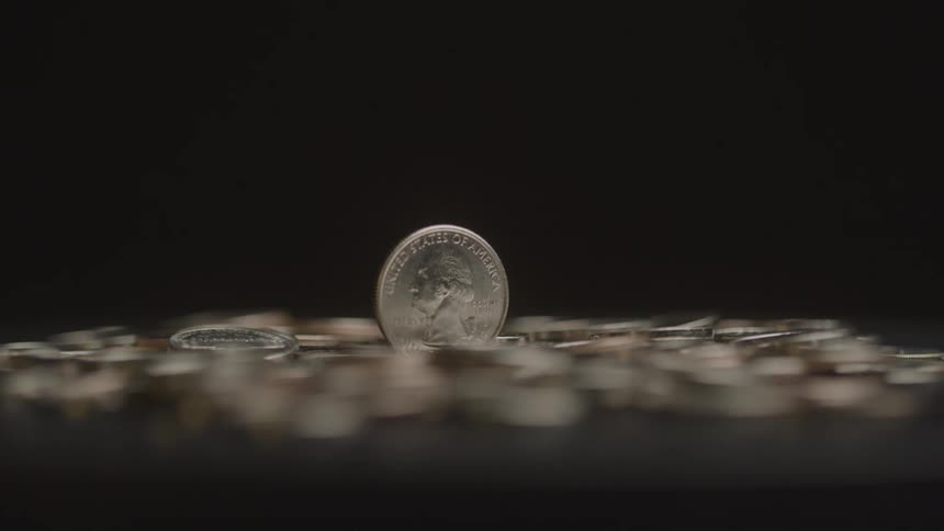 A single upright quarter stands among scattered coins against a dark background