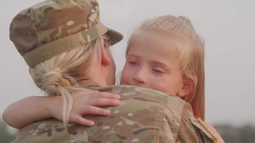 Mother in military attire lovingly hugging her little daughter