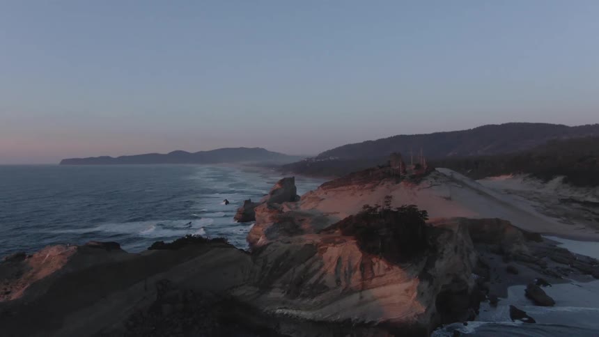 A scenic coastal landscape with rocky cliffs meets the ocean at dusk