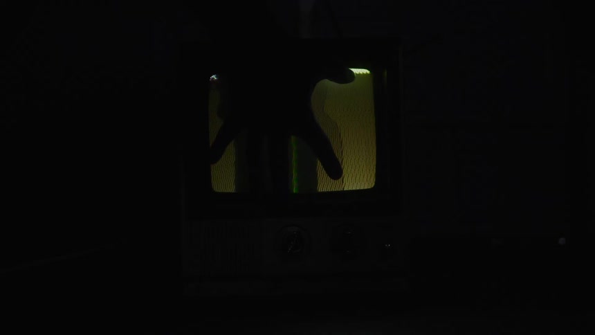 Hand approaches a small old television displaying colored static in the dark