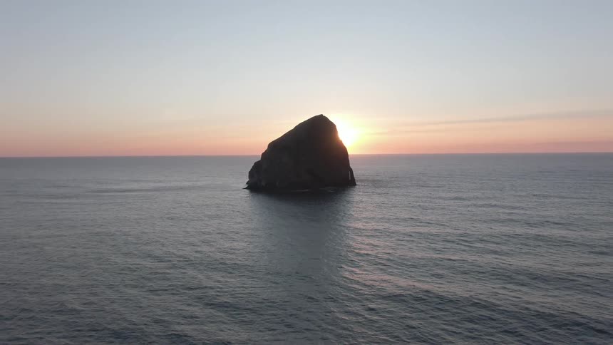 Landscape of an imposing rock in the middle of an ocean with the sunrise on the horizon