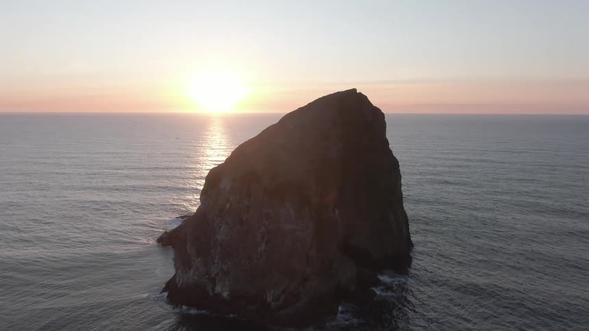 Rocky coast in the middle of the ocean with the sun on the horizon