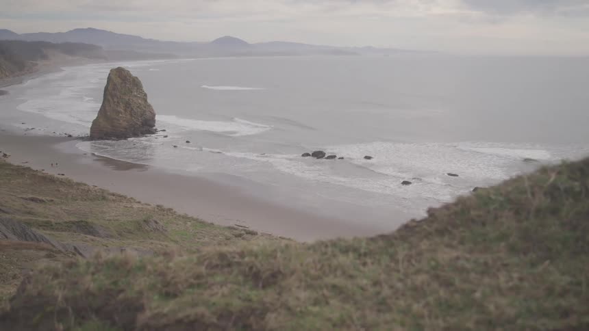 Aerial view of mountains along the coast as waves roll in to shore with rocks in the water