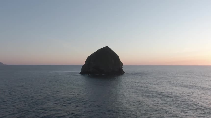 A large rock sits in the middle of the ocean around midday