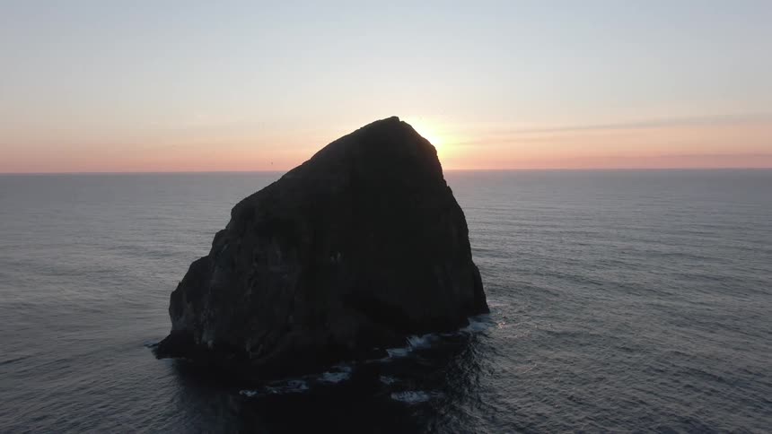 A large rock island rises from the ocean at sunset