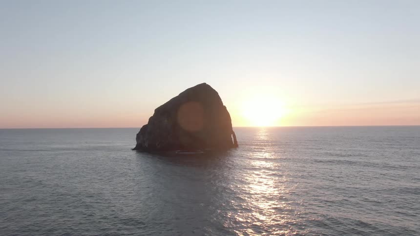 Rock in the middle of the sea with the sun rising on the horizon