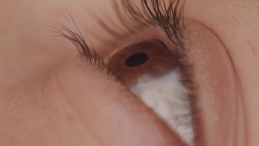 Extreme close up of a persons eyelid opening revealing brown eyes