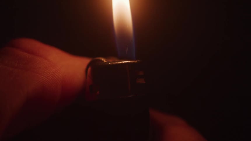 Hand lighting a lighter against a dark background