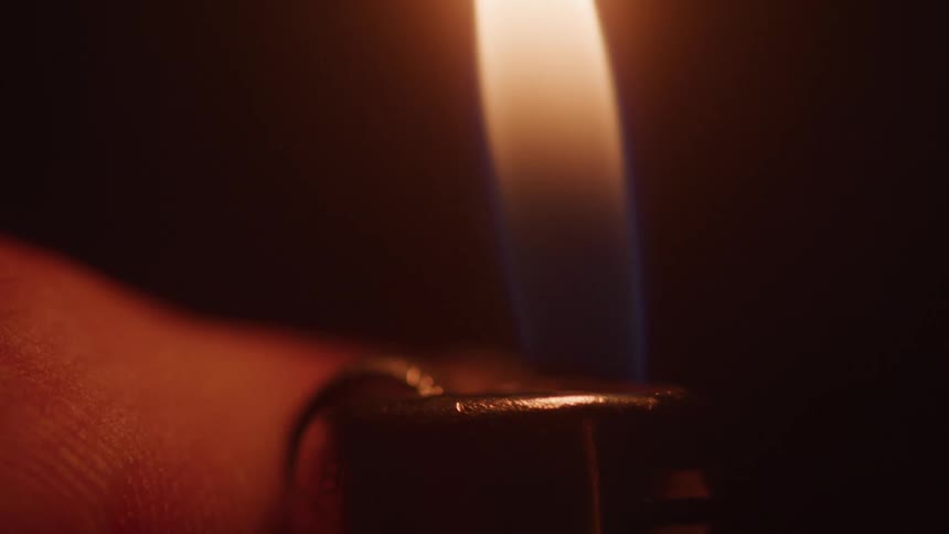 Close up of a hand lighter lit by a person in a dark environment