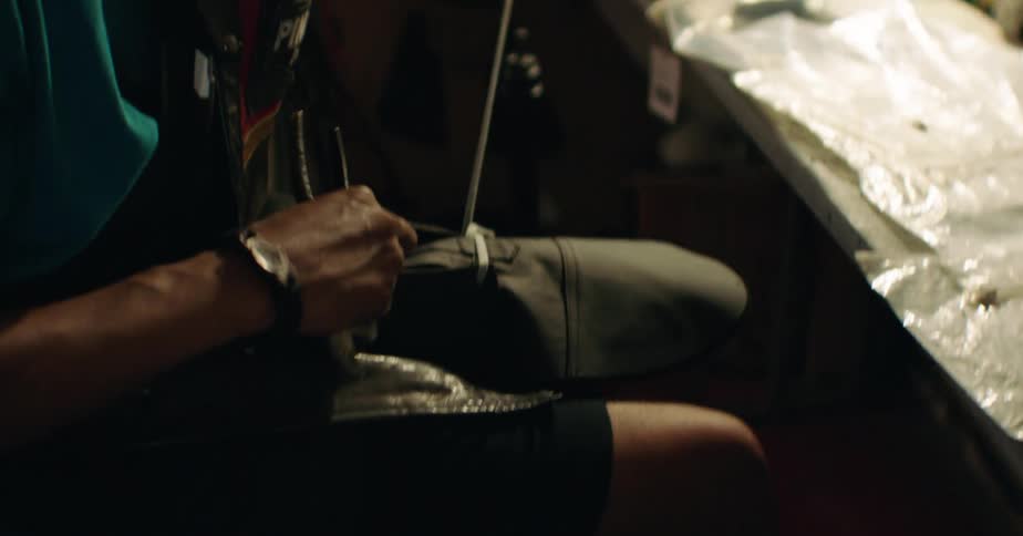Man working in an office containing many shoes manipulates laces with a tool