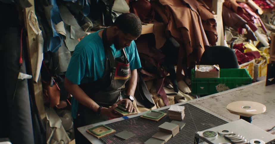 A shoemaker works on building a shoe sole inside a workshop around midday