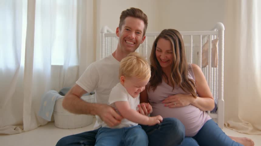 A happy young family sits on the nursery floor cuddling together with joyful expressions