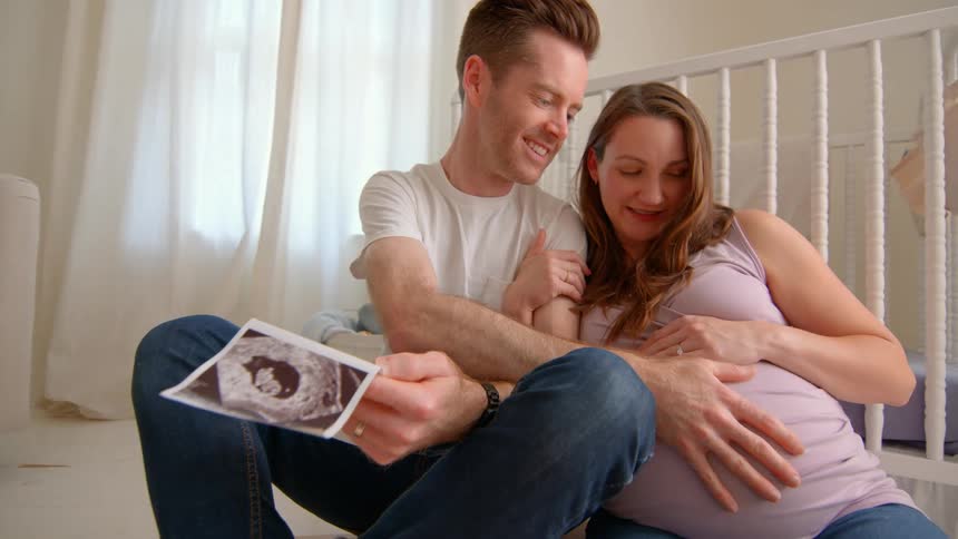 Couple sits happily with ultrasound man touching pregnant belly