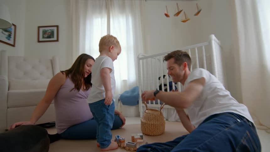 A young family plays on the nursery floor with their toddler and dog in a sunlit room