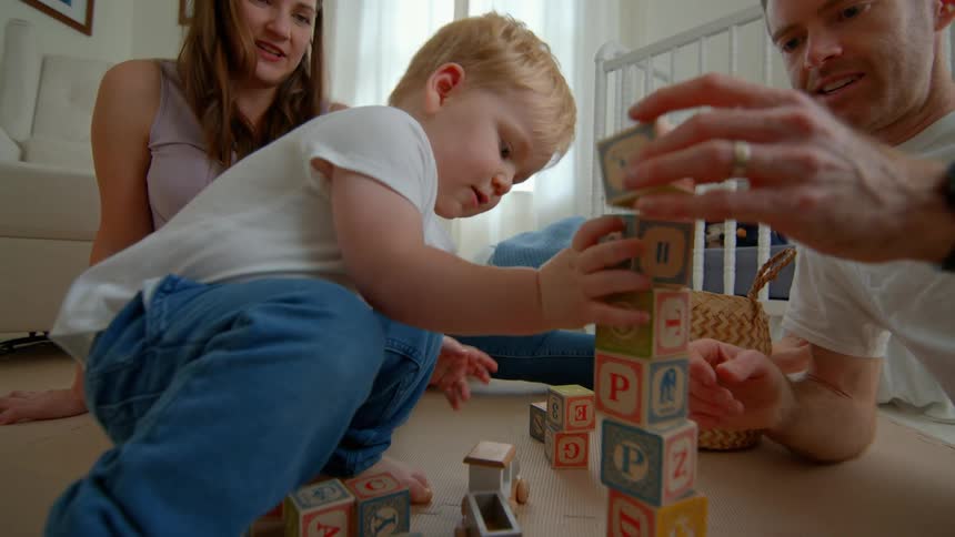 A young boy builds a block tower while playing with his parents on the floor
