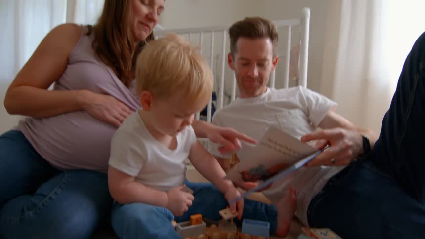 A family sits on the floor of a bright nursery playing with colorful wooden blocks and reading a book together